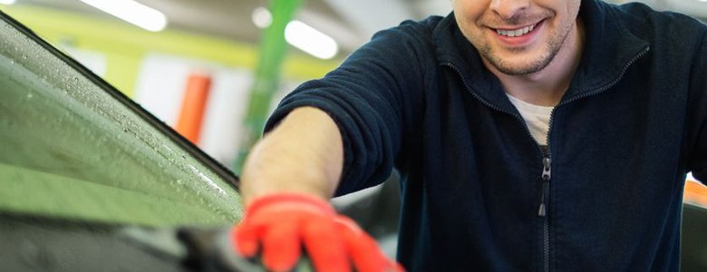 Mężczyzna czyści przednią szybę samochodu za pomocą rękawiczek.