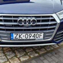 Zbliżenie na przednią osłonę chłodnicy i tablicę rejestracyjną niebieskiego pojazdu Audi.