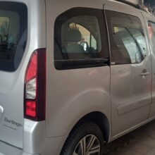 Srebrny Citroën Berlingo zaparkowany w garażu lub warsztacie, w tle widoczne środki czyszczące i sprzęt. Pokazano tył i lewą stronę pojazdu.